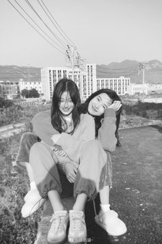 two young women sitting next to each other on top of a cement slab in front of a building