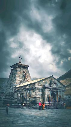 people are standing in front of an old building with a cloudy sky behind it and some mountains