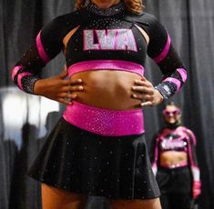 a woman in a pink and black cheerleader outfit is standing on stage with her hands on her hips