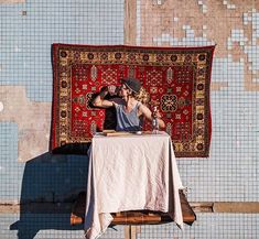 a woman sitting at a table in front of a rug and talking on the phone