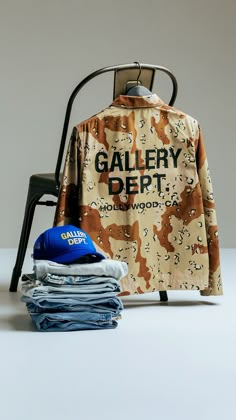 a shirt that is sitting on top of a chair next to some folded jeans and a blue hat