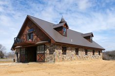 a stone building with a metal roof and two windows on the front, in an open field