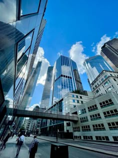 some people are walking down the street in front of tall buildings with glass windows on them