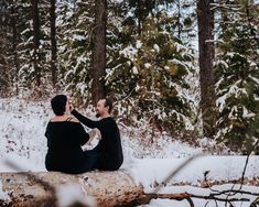 two people sitting on a log in the snow looking at each other and talking to each other