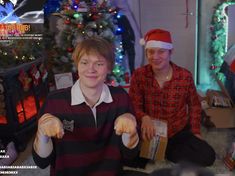 two young men sitting next to each other in front of a christmas tree with presents