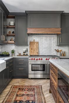 a kitchen with gray cabinets and an area rug in front of the stove top oven