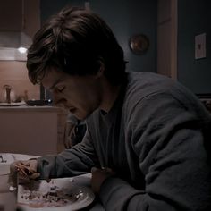 a man sitting at a table eating food from a plate with a knife and fork