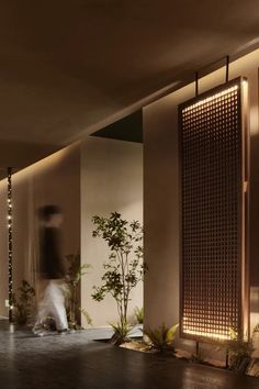 a person is walking past some plants in a room with lights on the walls and floor