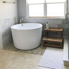 a large white bath tub sitting next to a window in a bathroom on top of a tiled floor