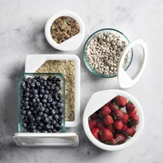 four bowls filled with cereal, berries and other foods on top of a marble counter