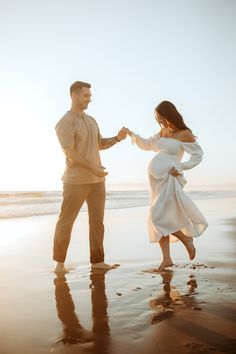 a man and woman dancing on the beach at sunset with their hands in each other's pockets