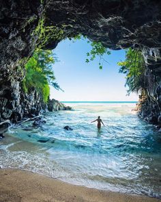 a person wading in the ocean through a cave