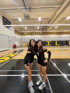 two young women standing on top of a basketball court next to an indoor volleyball court