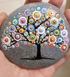 a hand holding a painted rock with a tree on it and colorful circles around the tree