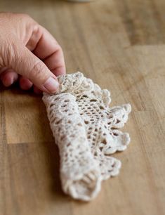 a person is holding a piece of crocheted material on a wooden table top