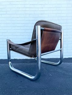 a brown leather chair sitting in front of a white brick wall with metal legs and armrests