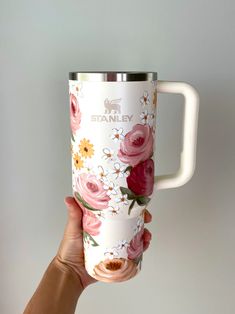 a hand holding a white coffee cup with pink flowers on the outside and gold rim