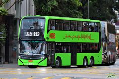 a green double decker bus is driving down the street with people on it's side