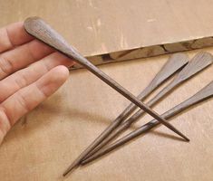 a person holding three wooden spoons on top of a table next to a pair of scissors