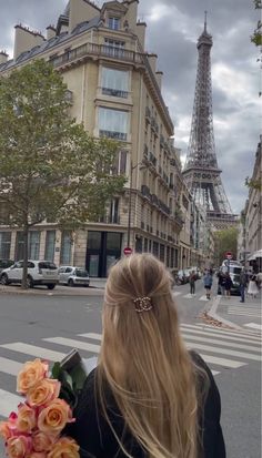 a woman is standing in front of the eiffel tower with flowers on her shoulder