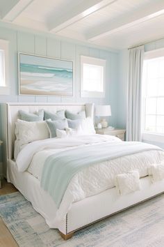 a white bed sitting in a bedroom next to two windows and a painting on the wall