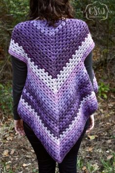 a woman wearing a purple and white crocheted shawl in front of trees