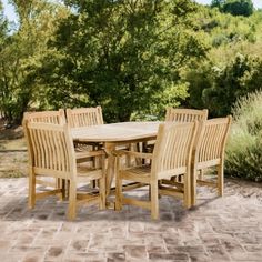 a wooden table and chairs sitting on top of a brick floored patio with trees in the background