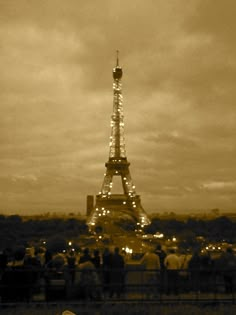 the eiffel tower lit up at night in sepia tone with people looking on