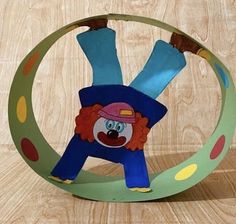 a paper sculpture of a clown hanging upside down on a circular object with polka dots around it