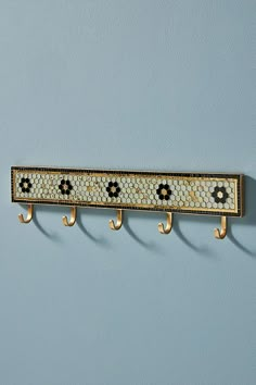 a wall mounted coat rack with three hooks and two flowers on each hook, against a pale blue wall