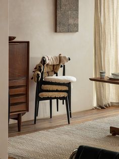 a dog sitting on a chair in a living room next to a table and dresser