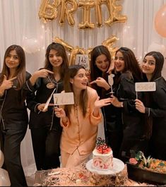 a group of women standing next to each other in front of a cake and balloons