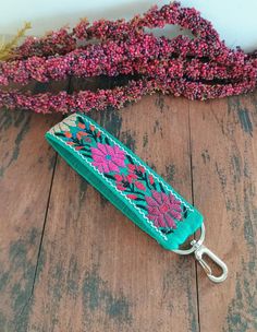 a green key chain with pink flowers on it sitting on top of a wooden floor