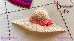 a crocheted hat with pink ribbon on it sitting on top of a piece of cloth