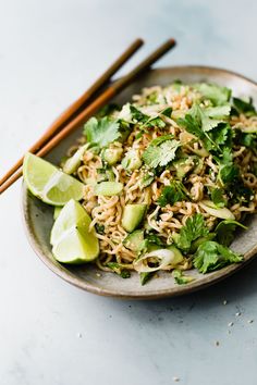 a plate filled with noodles and vegetables next to chopsticks on a white table