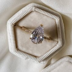 an engagement ring with a pear shaped diamond sits in a hexagonal display case