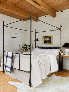 a bedroom with white bedding and wooden ceilinging, along with rugs on the floor