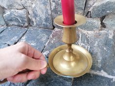 a person is holding a candle in front of a stone wall and a metal stand