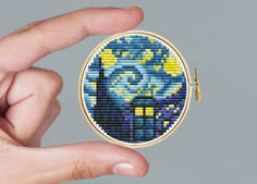 a hand is holding a small cross - stitch brooch