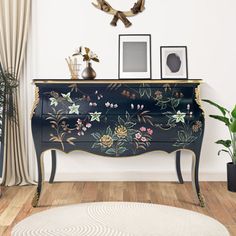 a black and gold painted dresser with flowers on it