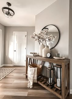 a wooden table sitting in the middle of a room next to a mirror and vase with flowers on it