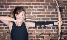 a young woman is practicing archery in front of a brick wall