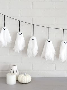 white ghost decorations hanging on a clothes line next to a candle and some pumpkins