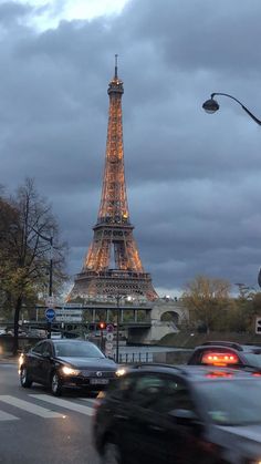 the eiffel tower is lit up at night, with cars driving down the street