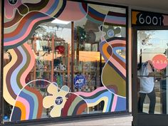 a man is standing in front of a store window that has colorful designs on it