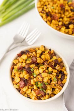 two bowls filled with corn and bacon on top of a white table next to green onions