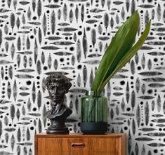 a green plant sitting on top of a wooden dresser next to a wallpaper covered in black and white designs