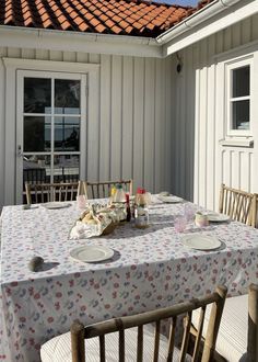 a table with plates and cups on it in front of a white house, next to an open patio door