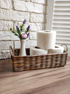 three rolls of toilet paper sitting in a basket next to a vase filled with flowers