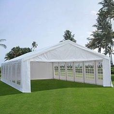 a large white tent set up in the middle of a grassy field with palm trees